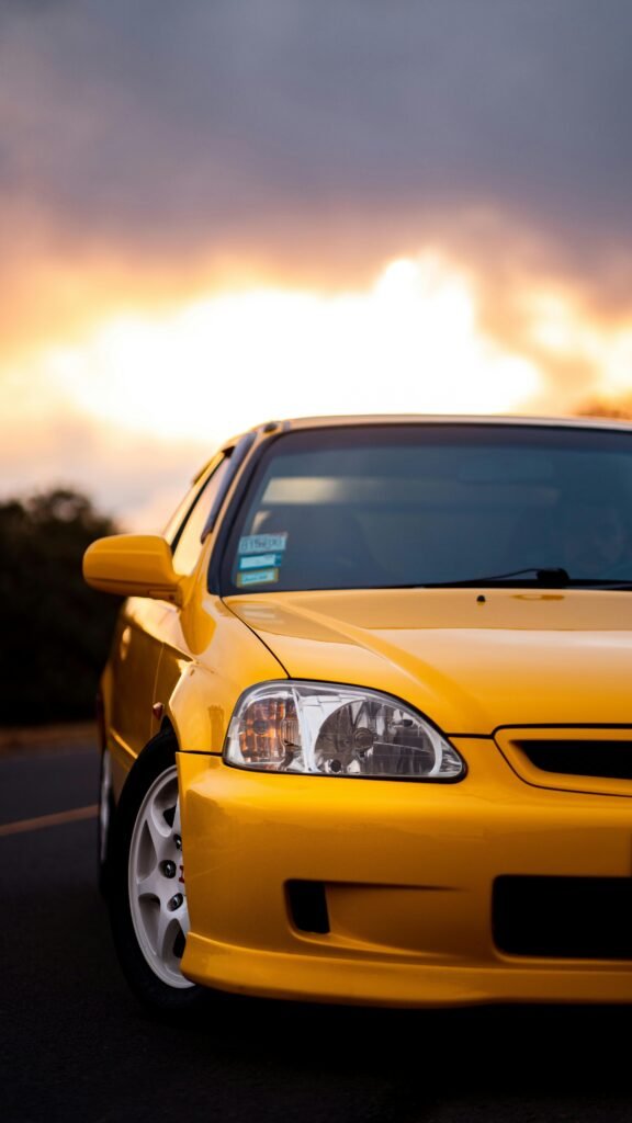 Vibrant yellow Honda Civic EK9 Type R captured close-up with a dramatic sunset backdrop.